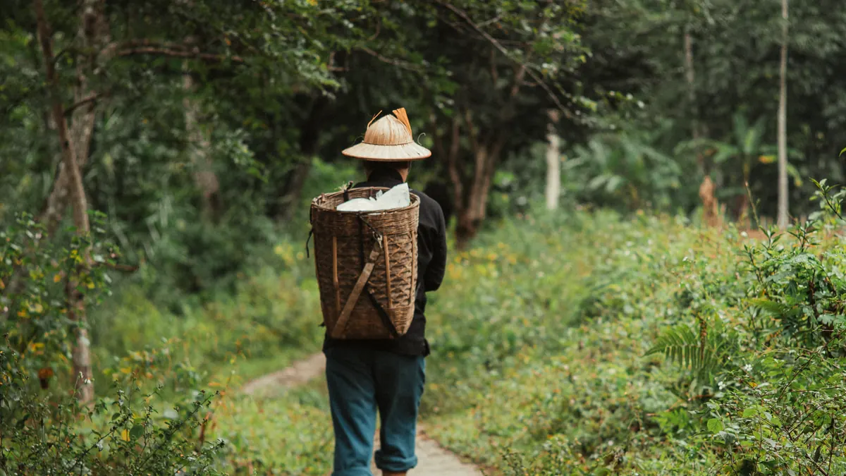 Petani membawa keranjang anyaman berjalan di jalan setapak hutan